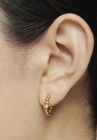 Pendientes de aro de oro con una superficie texturizada y rugosa, adornados con pequeñas perlas redondas a lo largo de la circunferencia, colocados en la oreja.