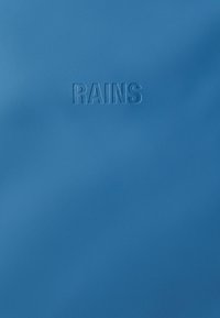 Vízálló kék anyag, amelyen a "RAINS" logó dombornyomott, sima tapintású és letisztult, minimalista dizájnnal rendelkezik.