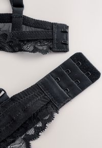 Mustad pitsrinnahoidja rihmad, millel on sile kangaspõhi ja tekstuuriga pitsdetailid, kinnituvad haagi ja silma kinnitustega reguleeritava sobivuse tagamiseks.