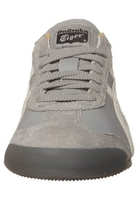 Šedé tenisky vyrobené z velurové a kožené materiály, s kulatou špičkou, šněrováním a logem na jazyku. Mají texturovanou podrážku pro lepší přilnavost.