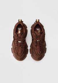 Brune sneakers med en struktureret overdel, der har glitrende detaljer, en tyk sål og et træktab. Omfatter snøresystem og logo detalje.