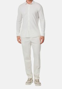 Bílá košile s dlouhým rukávem na knoflíky v kombinaci s odpovídajícími kalhotami a teniskami s béžovými akcenty; hladká tkanina, přizpůsobený střih a čistý design.