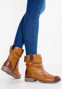 Bottines en cuir marron avec un haut décontracté, une fermeture éclair latérale et un petit talon en bois, associées à un jean bleu ajusté.