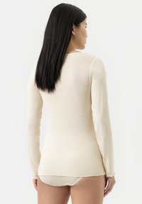 Un haut en crème à manches longues, fabriqué dans un tissu doux, avec un col rond et une conception ajustée. Pas de motifs ni de pièces métalliques visibles.