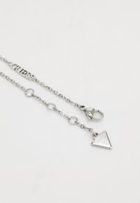 Silver chain necklace featuring an adjustable design, round links, a clasp closure, and a triangular charm with engraved brand name.