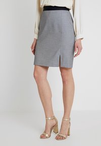 Harmaa kynähame, jossa on musta vyötärönauha ja etuhalkio. Kankaassa on hienovarainen rakenne. Yhdistetty metallinhohtoisiin kultaisiin paksupohjaisiin sandaletteihin.