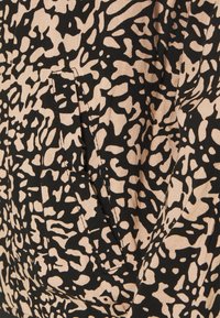 Tissu beige avec des taches noires abstraites irrégulières ressemblant à celles d’un léopard et un détail de couture visible.