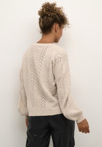 Beige strikket sweater med løstsiddende pasform, der har et chevronmønster og teksturerede ærmer. Ribstrikkede manchetter og bund tilføjer detaljer til designet.