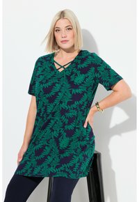 Marineblå tunika med grønne bregneprint, korte ærmer, V-hals med krydsgående detaljer, parret med mørke leggings og et guldarmbånd.
