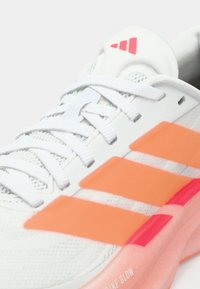 Λευκό αθλητικό παπούτσι με γκρι πάνω μέρος από δίχτυ, πορτοκαλί ρίγες και ροζ διαφανές πέλμα. Διαθέτει λευκά κορδόνια και λογότυπο adidas στη γλώσσα.