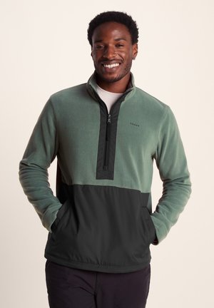 Fleece pullover with a green top and black bottom, zip neck, two pockets, and a logo on the chest. Soft texture and relaxed fit.