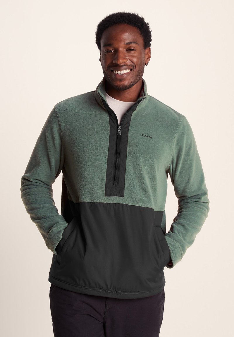 Fleece pullover with a green top and black bottom, zip neck, two pockets, and a logo on the chest. Soft texture and relaxed fit.