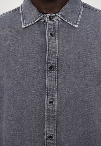 Harmaa denimpaita, jossa on terävä kaulus, edessä nappikiinnitys mustilla nappeilla sekä teksturoitu kangas, jossa on hienovarainen kuosi.