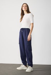 Pantaloni cargo navy con polsini elasticizzati, tasche laterali e vita con cordoncino regolabile, abbinati a un top rigato bianco testurizzato.