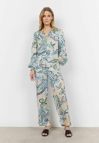 Costum în două piese cu model, având o bază bej deschis și desene intricatelor în nuanțe de albastru și verde în stil paisley, cu mâneci lungi și pantaloni cu croială lejeră.