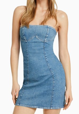 Bezramiankowa, jasnoniebieska mini sukienka z denimu z widocznymi przeszyciami, noszona przez osobę o długich blond włosach, stojącą na białym tle.