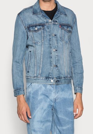 Homme portant une veste en denim bleu clair avec fermeture à boutons et un jean assorti en denim bleu clair.