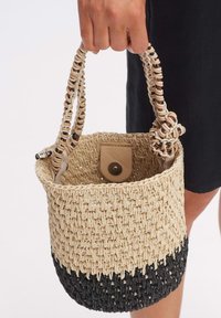 Geweven stro bucket bag met tan en zwarte secties, voorzien van twee gevlochten handvatten en een leren drukknoopsluiting aan de binnenkant.