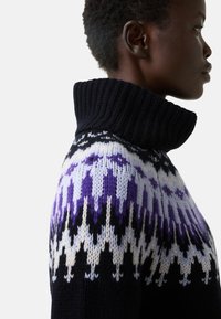 Knit sweater with a high ribbed collar; features a geometric pattern in purple, white, and black on a dark background.