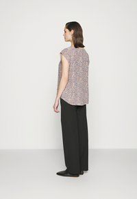 Top com padrão floral, mangas curtas, corte descontraído e hemínio arredondado, combinado com calças pretas de cintura alta e sapatos pretos de bico.