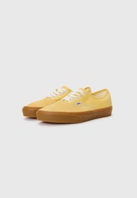 Yellow suede low-top sneakers with white laces and a rubber gum sole. Features a small logo tag near the outer side. Smooth texture.