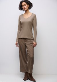 Halenka s dlouhými rukávy a výstřihem do V z měkkého taupe materiálu, spárovaná s volnými, texturovanými hnědými kalhotami a hnědými kotníkovými botami. Čisté linie a uvolněný střih.