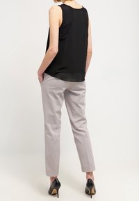 Černý top bez rukávů s krajkovými detaily, spárovaný se světle šedými slim kalhotami a černými vysokými podpatky, pohled zezadu.