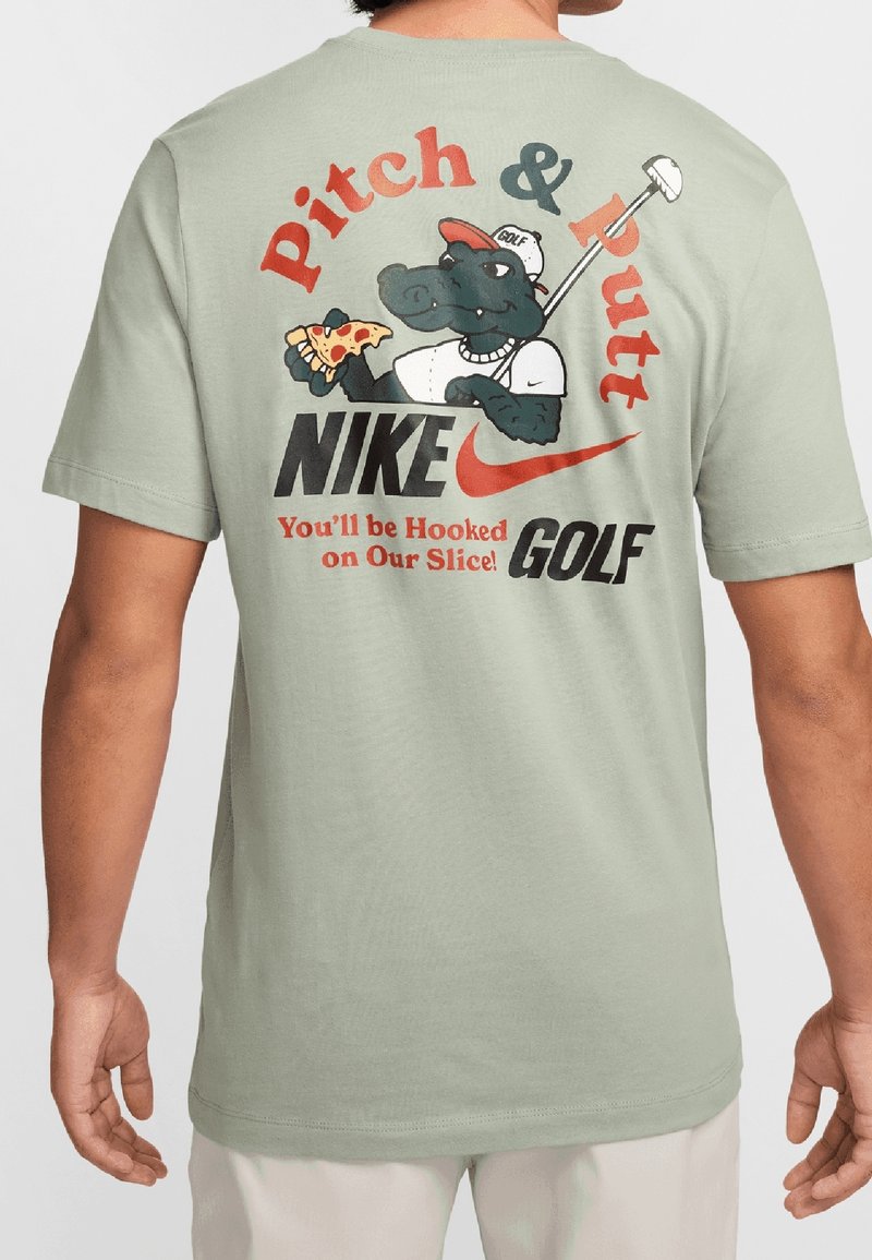 Světle zelené bavlněné tričko s grafikou aligátora držícího pizzu, se silným textem "Pitch & Putt" a "Nike Golf" v výrazných barvách.