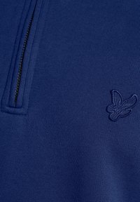 Pullover blu navy con collo a zip, realizzato in tessuto strutturato. Presenta un piccolo logo ricamato a forma di uccello sul petto.