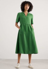 Rochie din in verde, cu mâneci scurte, guler și talie strânsă. Dispune de buzunare laterale și o siluetă fluidă în formă de A.