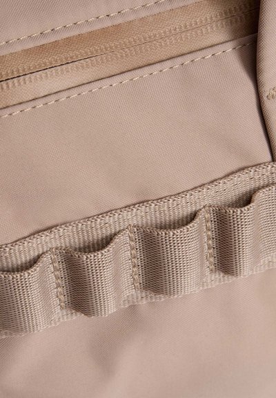 Εσωτερικό μπεζ υφασμάτινης τσάντας με λείο φερμουάρ και έναν τσέπη-οργανωτή με ραβδώσεις και ελαστικές θηλιές για την ασφάλιση μικρών αντικειμένων.