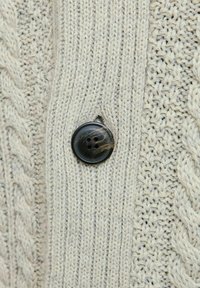 Gilet en tricot beige clair avec un motif en câble, un bouton noir brillant à quatre trous et des détails de couture texturés.