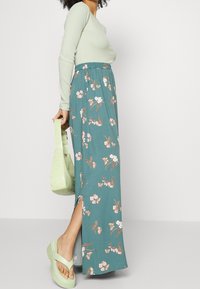 Maksihame teal-värissä kukkakuosisena, jossa on sivuleikkaus. Pitkähihaista yläosaa vaaleanvihreänä ja paksuja mintunvärisiä sandaaleja. Alligaattorin tekstuurilla varustettu käsilaukku.