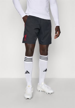 Svarte treningsshorts med rødt Liverpool FC-logo, kombinert med hvite knelengde sokker med svarte striper og hvite fotballsko.