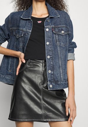 Kobieta ubrana w niebieską kurtkę dżinsową na czarnym krótkim topie i czarną skórzaną mini spódniczkę, z ręką na biodrze.