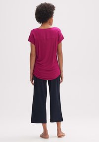 Fuchsiová short-sleeve blůza s volným střihem a zaobleným lemem, spárovaná s volnými černými širokými kalhotami. Hladká látka s jemným leskem.