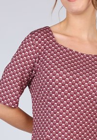 Bordeauxfarbenes Oberteil mit floralem Muster in Pink- und Weißtönen. Das Design umfasst kurze Ärmel und einen quadratischen Ausschnitt. Glatte Stofftextur.