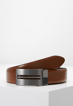 Ceinture en cuir marron avec une boucle rectangulaire en métal argenté présentant deux fentes horizontales découpées, enroulée sur une surface blanche.