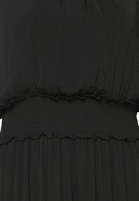 Robe noire en gros plan montrant une taille smockée élastique et des détails de tissu froncés au-dessus et en dessous de la ceinture.