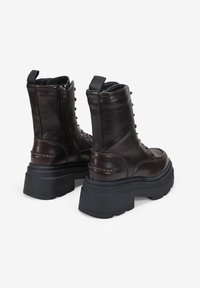 Botines de cuero marrón oscuro con cremalleras laterales, suelas de plataforma negras gruesas, parte delantera con cordones y tiradores en la parte trasera.