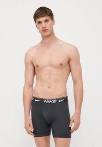 Mörkgrå Nike kalsonger med svart midjeband som har vit logotyp, slät textur och korta ben, designade för komfort och stöd.