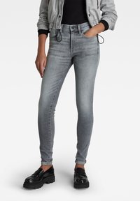 Vaqueros skinnies grises con un acabado desvanecido, diseñados con una cintura alta, presillas para cinturón, bolsillos frontales y un corte ajustado. Combinados con mocasines negros.