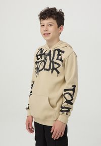 Felpa beige con cappuccio e testo grafico nero sulla parte anteriore e sulle maniche. Presenta una tasca a marsupio e polsini a costine. Materiale in misto cotone.