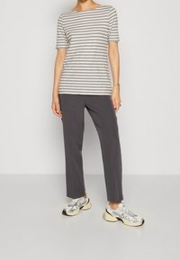 Camiseta a rayas en gris y crema con mangas cortas, combinada con pantalones grises y zapatillas deportivas plateadas, con acentos brillantes.