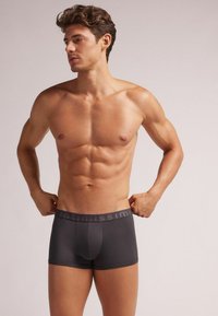 Grå boxershorts med tætsiddende design, elastisk taljehåndtag med mærkenavn, glat tekstur og tætsiddende skæring omkring lårene.