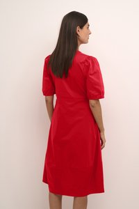 Rochie roșie, până la genunchi, dintr-un material neted. Dispune de mâneci scurte, pufoase și un corp ajustat cu o fustă evazată. Fără modele vizibile.