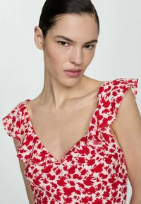 Květinové šaty s červenými květy na světlém pozadí, s volánovými rukávy a výstřihem do V. Hladká textilie a přiléhavý střih.