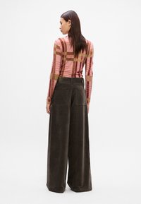 Haut à col montant et manches longues avec un motif à carreaux rose et marron, associé à un pantalon en velours côtelé vert foncé à jambes larges avec des poches arrière.