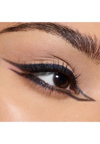 Close-up of an eye with a bold black eyeliner design, featuring elongated flicks and thick lashes on a smooth, lightly textured eyelid.
