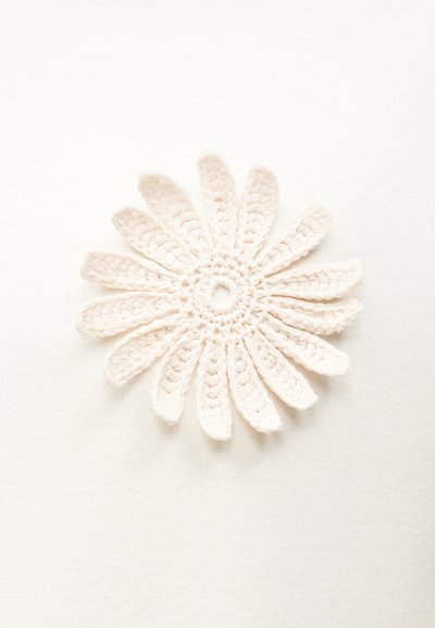 Πλεκτό μαργαρίτα με δώδεκα πέταλα από εκρού νήμα σε λευκό υφασμάτινο φόντο.